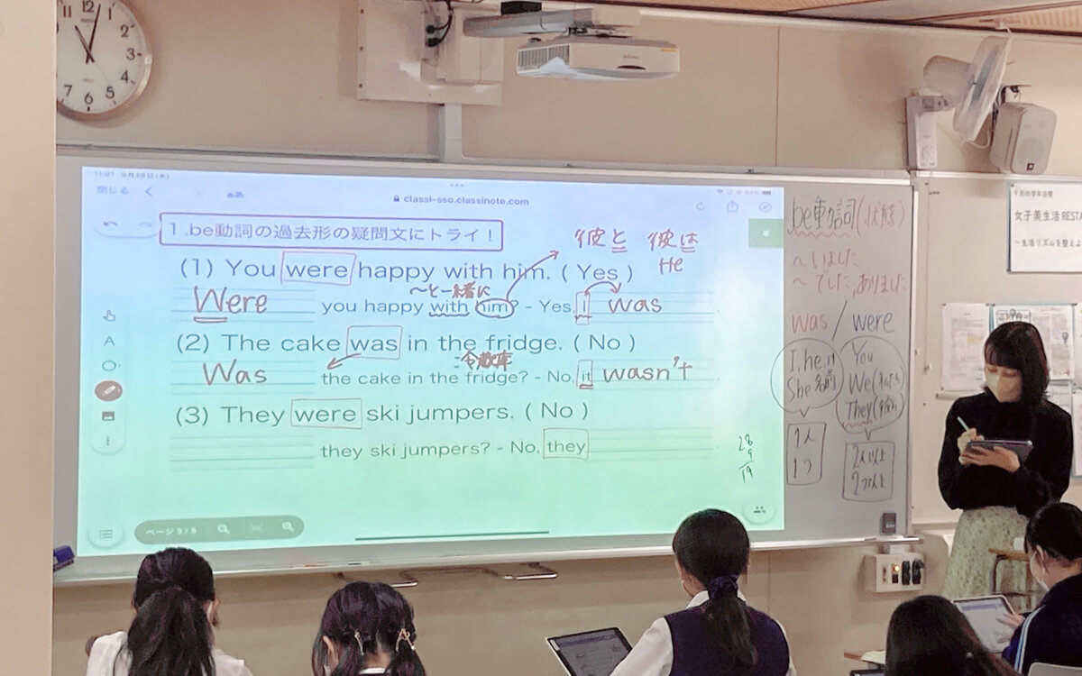 英語の授業でプロジェクター「ワイード」（電子黒板）を使う先生_タブレットに書き込みながら